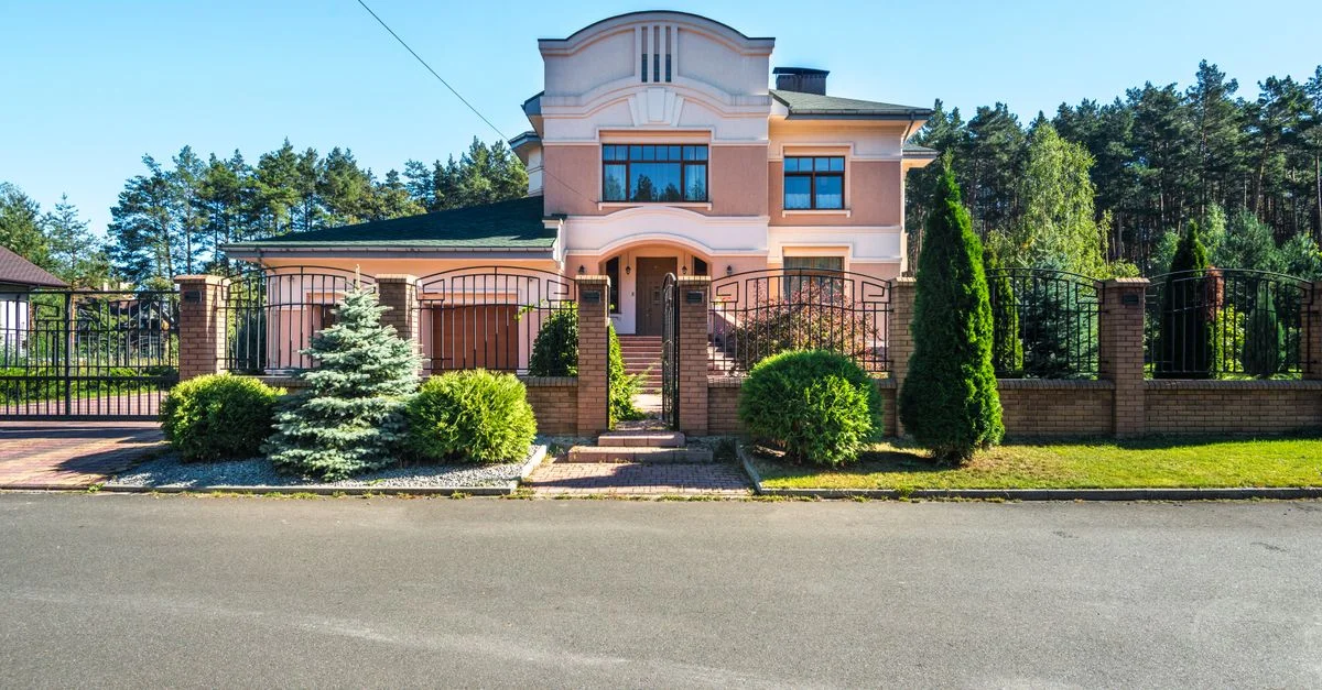Belle maison de luxe en banlieue avec jardin paysager et entrée sécurisée par un portail par une journée ensoleillée.