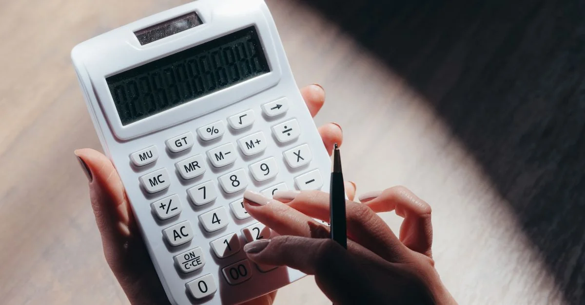 Des mains tenant une calculatrice et un stylo pour des calculs financiers dans un environnement bien éclairé.