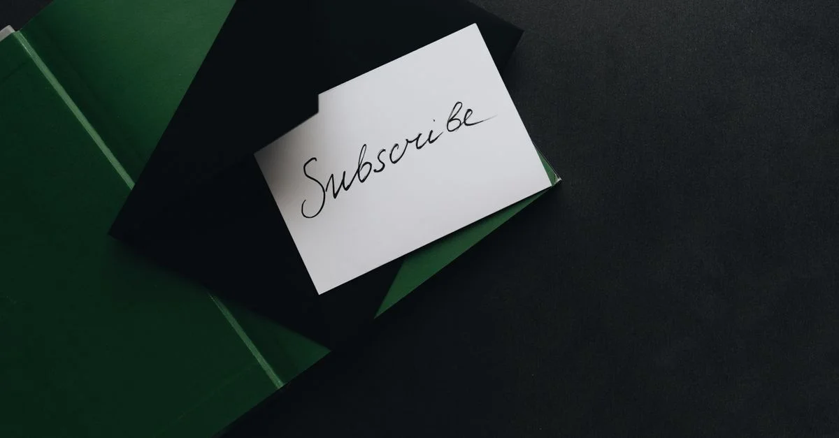 Une image minimaliste d'une carte 'S'abonner' dans une enveloppe verte sur un fond sombre.