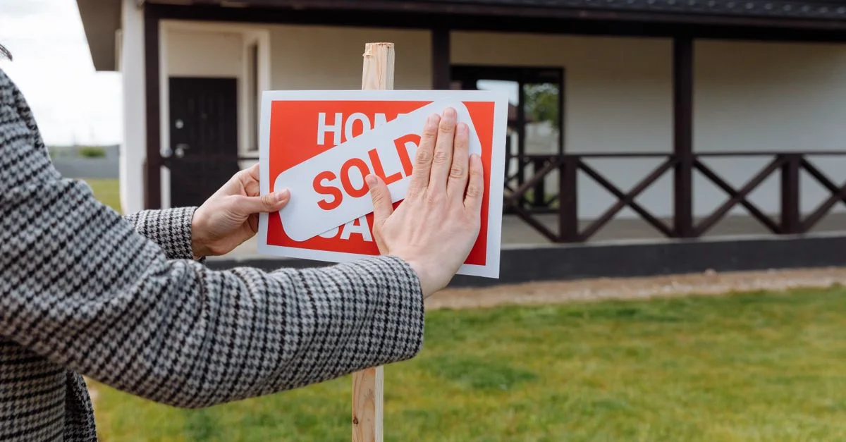 Gros plan sur des mains plaçant un autocollant 'vendu' sur un panneau devant une nouvelle maison.