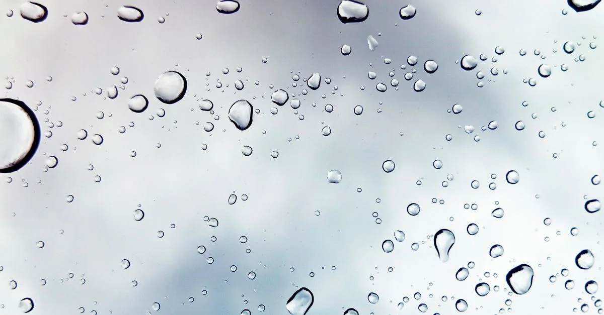 Des gouttes de pluie sur une fenêtre contre un ciel nuageux, créant une ambiance paisible.