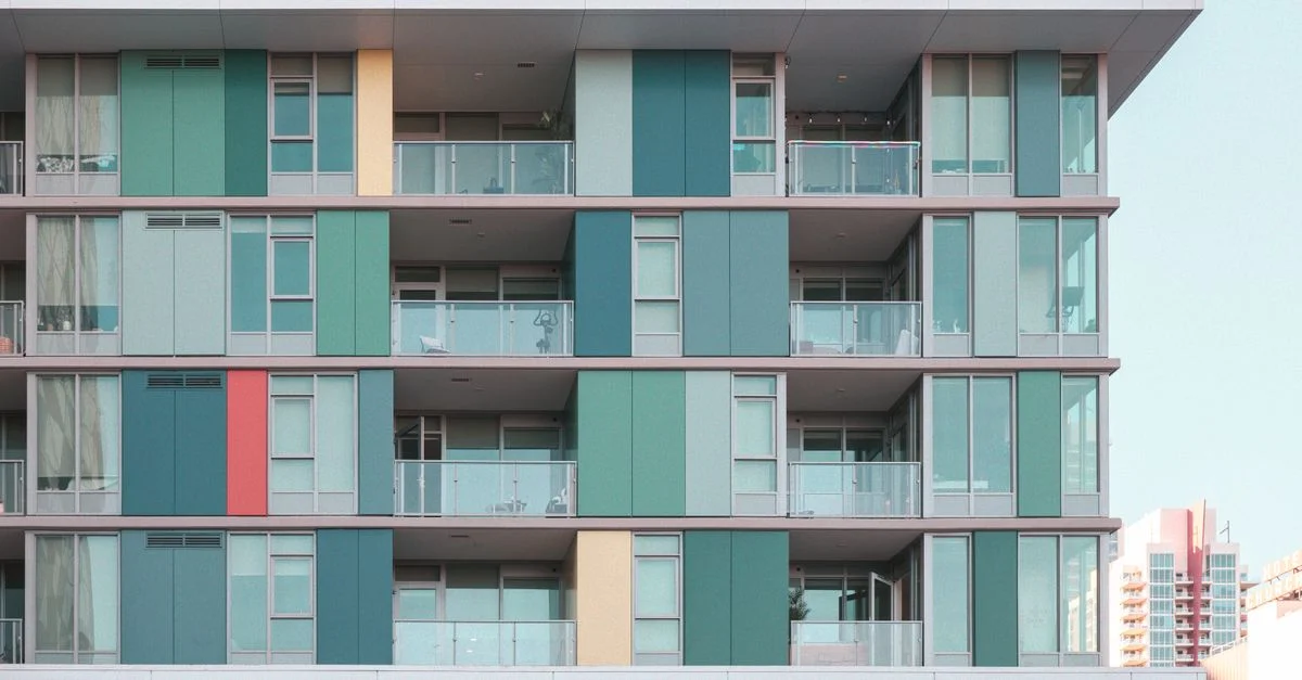 Façade d'immeuble moderne et dynamique avec balcons en verre sous un ciel bleu clair.