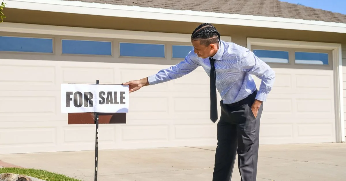 Agent immobilier professionnel installant un panneau à vendre devant une maison.