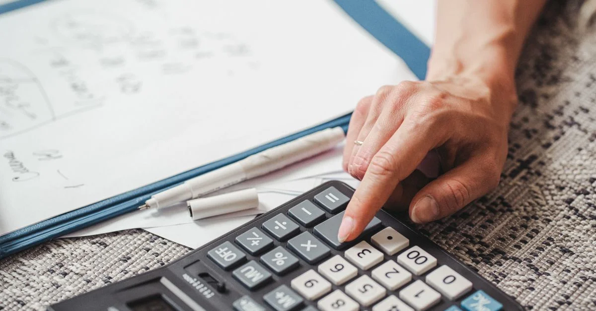 Une main utilisant une calculatrice sur des documents, indiquant un calcul ou une analyse financière.