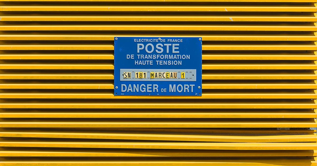 Gros plan d'une grille industrielle jaune avec un panneau d'avertissement haute tension bleu.
