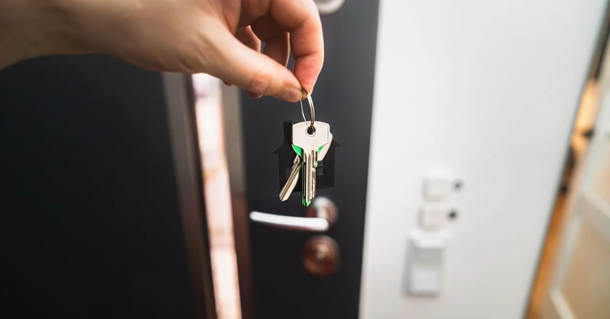 Gros plan d'une main tenant des clés devant une porte ouverte, symbolisant l'accession à la propriété.