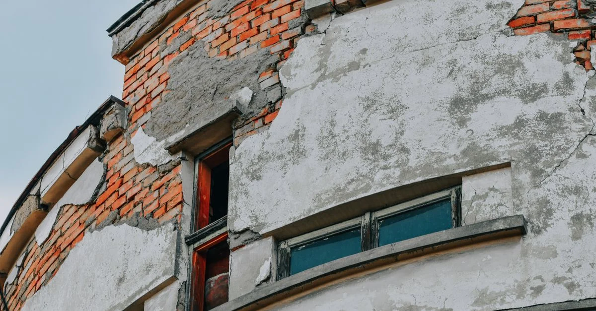 Gros plan d'une façade de bâtiment en brique vieillie montrant des fissures et une détérioration.