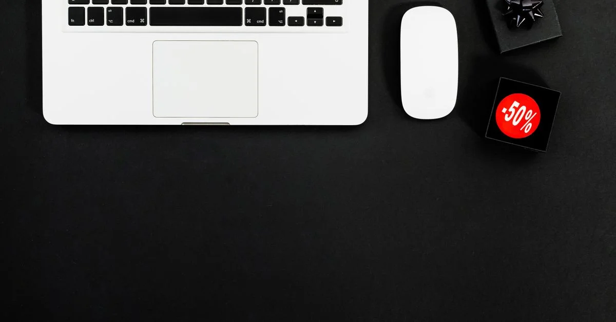 Mise en scène minimaliste avec un ordinateur portable et des articles de shopping avec des étiquettes de 50 % de réduction.