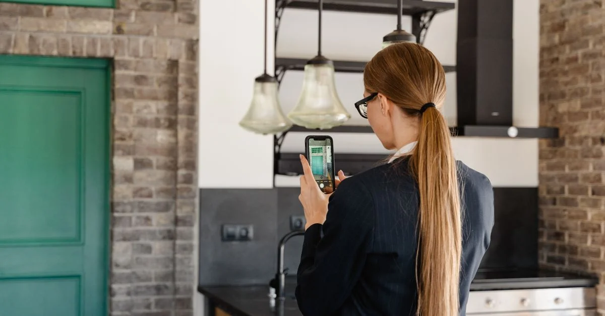 Vue de dos d'une femme aux longs cheveux prenant une photo avec un smartphone dans une cuisine élégante.