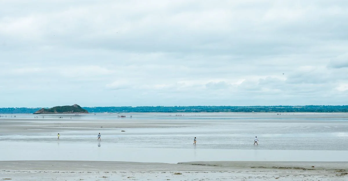Vue panoramique des plages à marée basse du Mont-Saint-Michel, en Normandie, avec des promeneurs au loin.