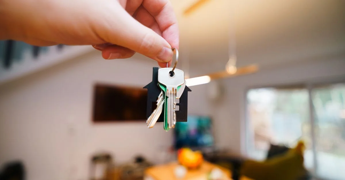 Une main tient des clés avec un porte-clés de maison à l'intérieur d'un espace de vie moderne et bien éclairé.