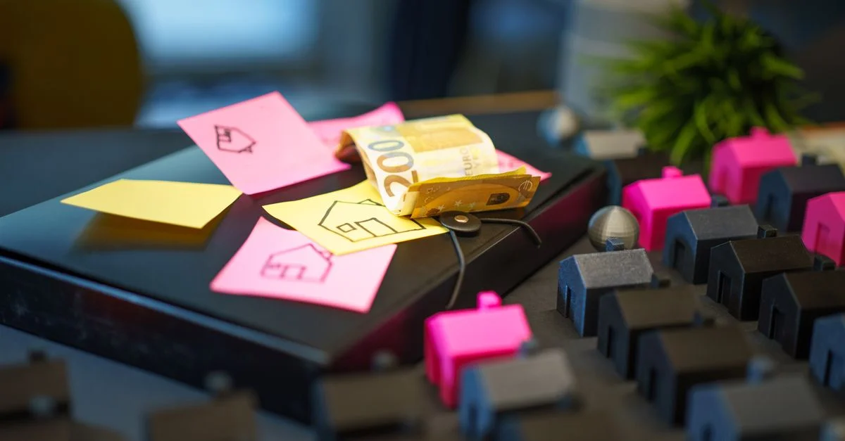 Billets euro sur ordinateur portable avec des post-it et des modèles de maison, symbolisant l'investissement immobilier.