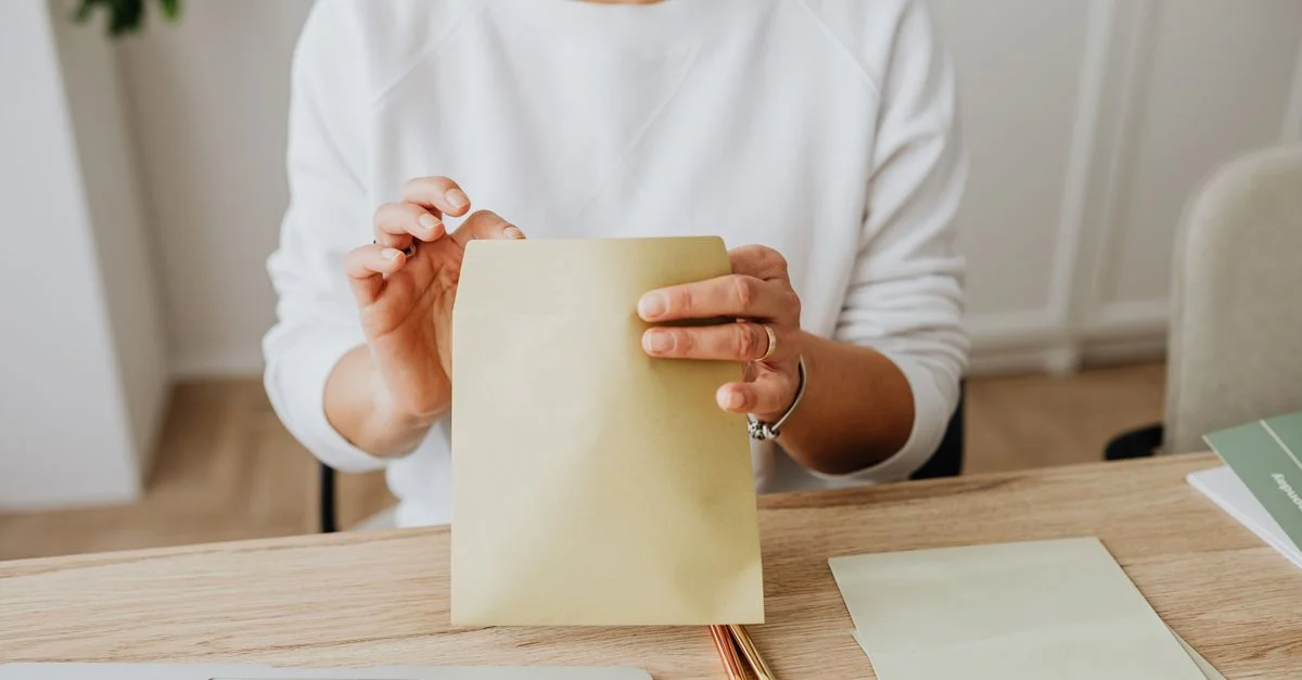 Gros plan sur une femme scellant une enveloppe brune assise à un bureau en bois à l'intérieur.