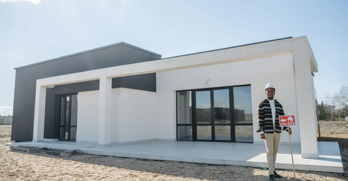 Un agent immobilier se tient avec un panneau à vendre devant une maison moderne.