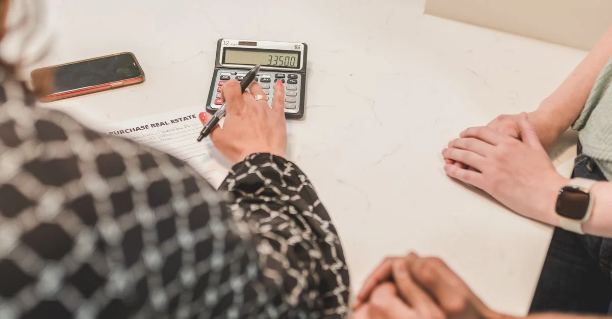 Gros plan sur des mains pendant une transaction immobilière avec une calculatrice et un document d'achat sur la table.