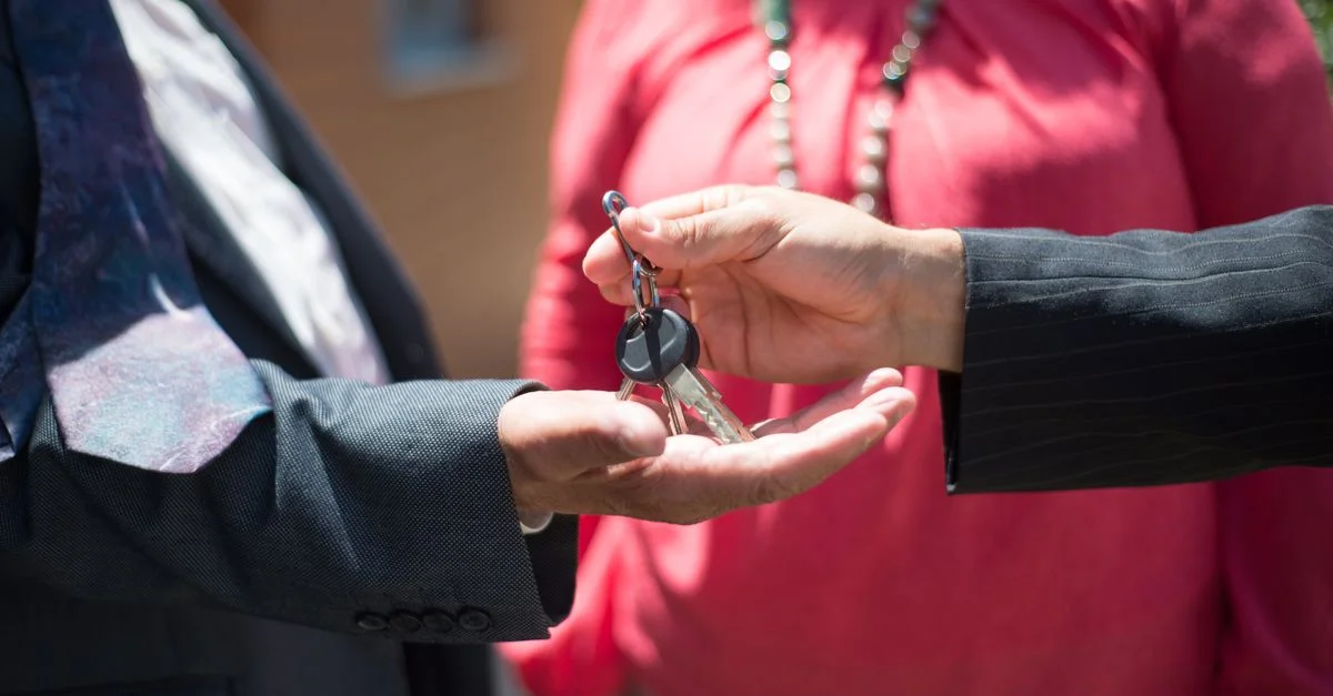 Gros plan de deux personnes échangeant des clés, symbole d'une transaction immobilière.